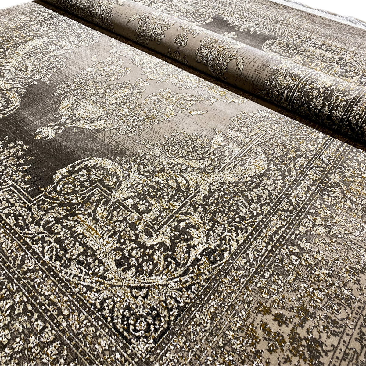Detalle de una alfombra con un motivo barroco dorado-beige sobre un fondo gris oscuro