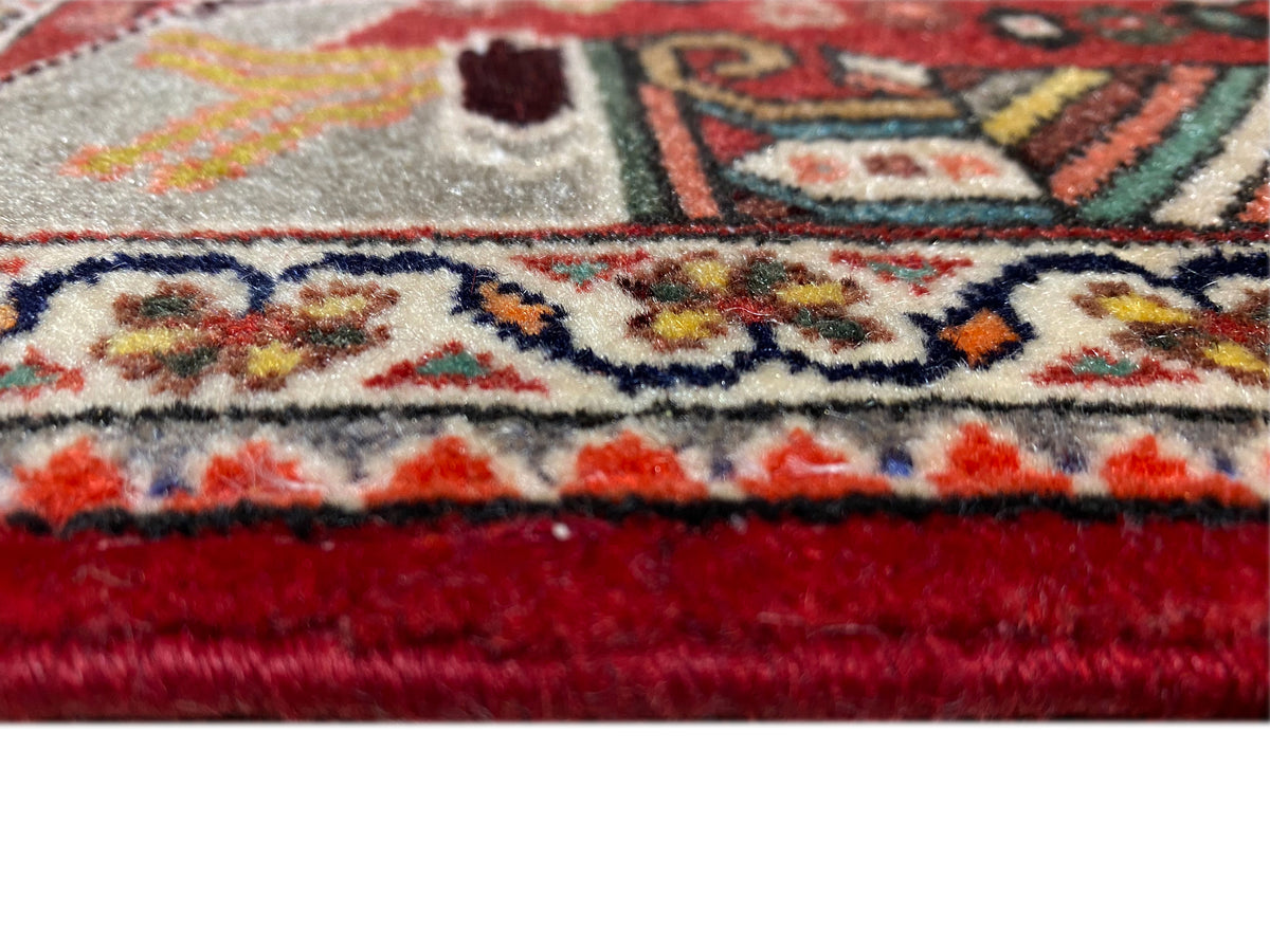 Primer plano: borde de alfombra con flecos, remate rojo y un denso diseño ornamental