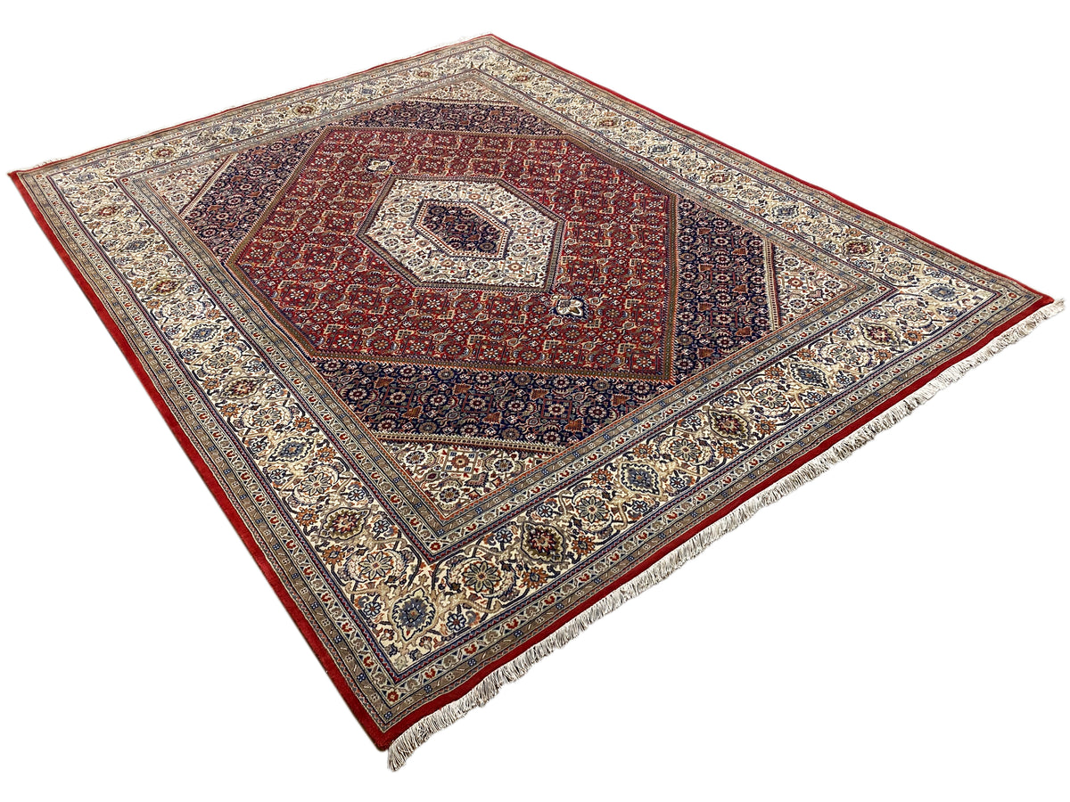 Alfombra con motivo central rojo, líneas decorativas claras y un amplio borde con motivos ornamentales