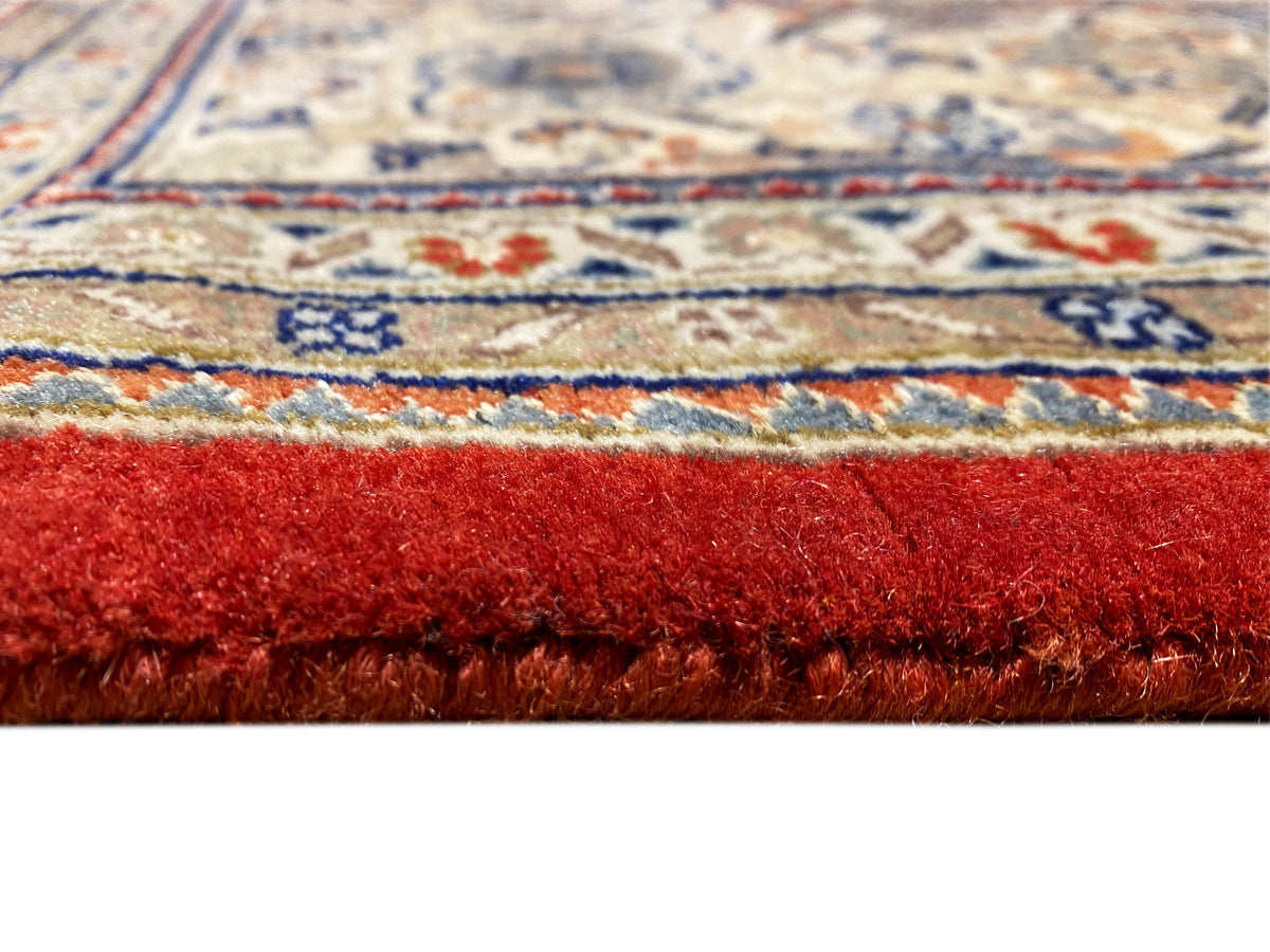 Borde de alfombra con flecos y pelo de color marrón rojizo; debajo, una cenefa decorativa multicolor