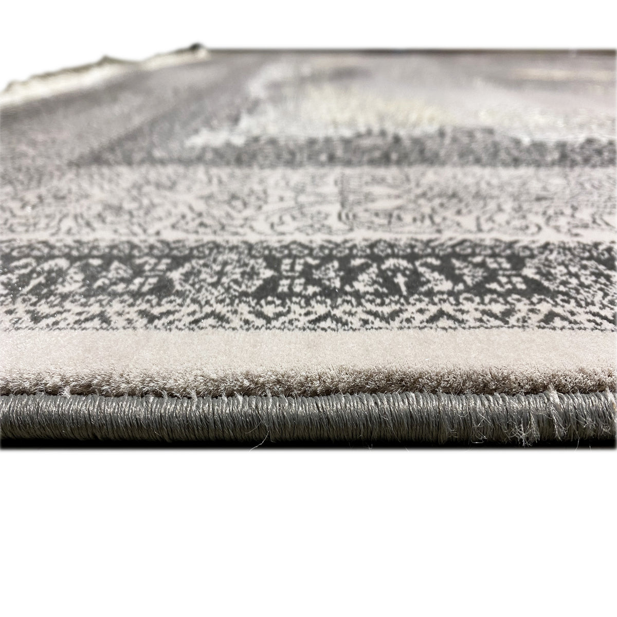 Primer plano del borde y el motivo floral: remate de flecos en la alfombra gris