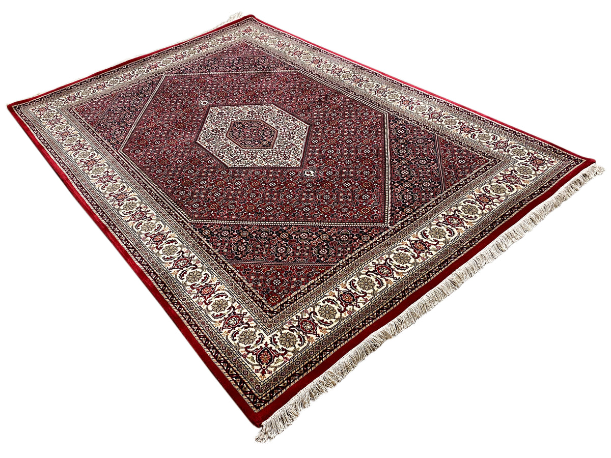 Alfombra roja con medallón central, ornamento geométrico y borde de color crema
