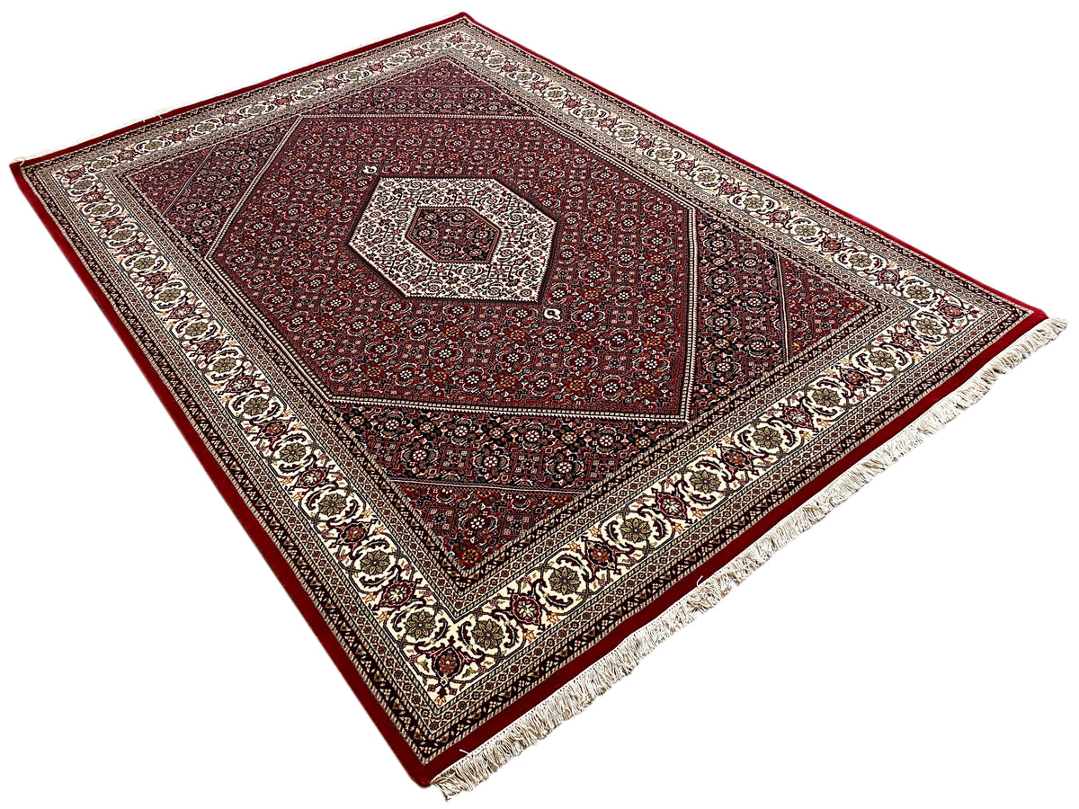 Alfombra roja de Bidjar extendida, con medallón en el centro, cenefa y flecos