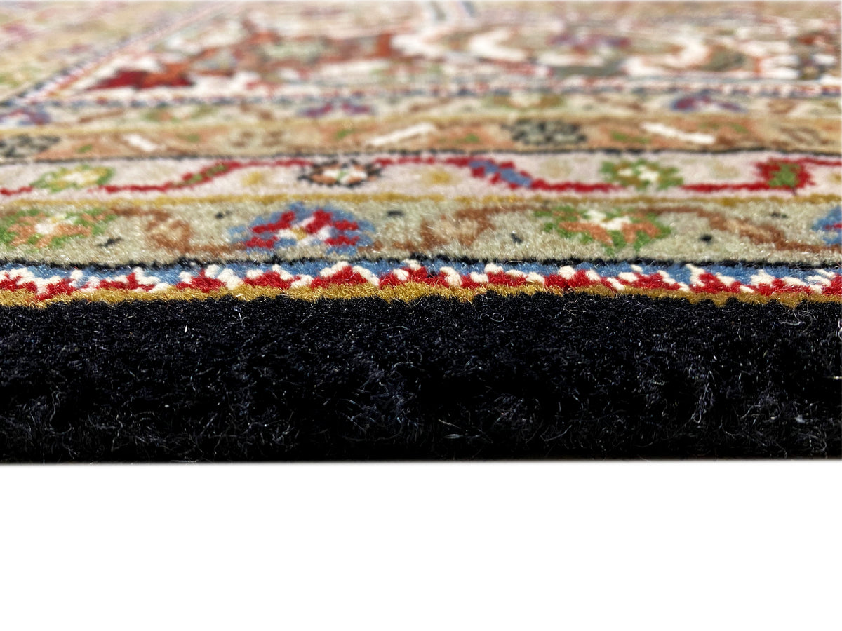 Primer plano: alfombra Indo-Tabriz marrón con una franja ornamental multicolor y flecos.