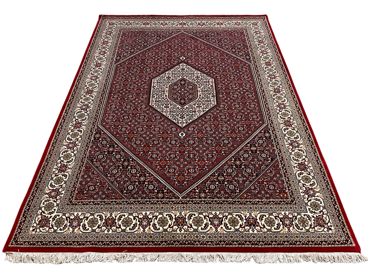 Alfombra roja con medallón central, ornamento simétrico y flecos en el borde