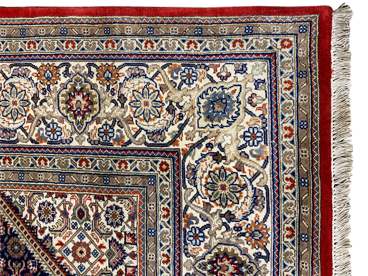 Esquina de alfombra con flecos: campo de diseño claro, borde rojo y franjas con motivos azules