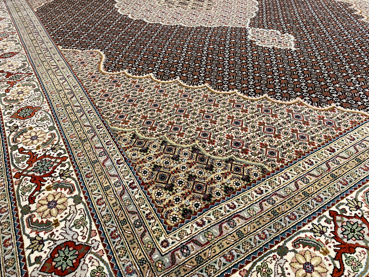 Esquina de una alfombra marrón oscuro con cenefa ornamental y detalles florales