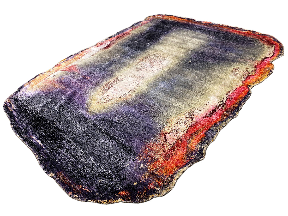 Vista de la alfombra de diseño: lila-azul con zonas claras de color crema y acentos naranjas, bordes irregulares.