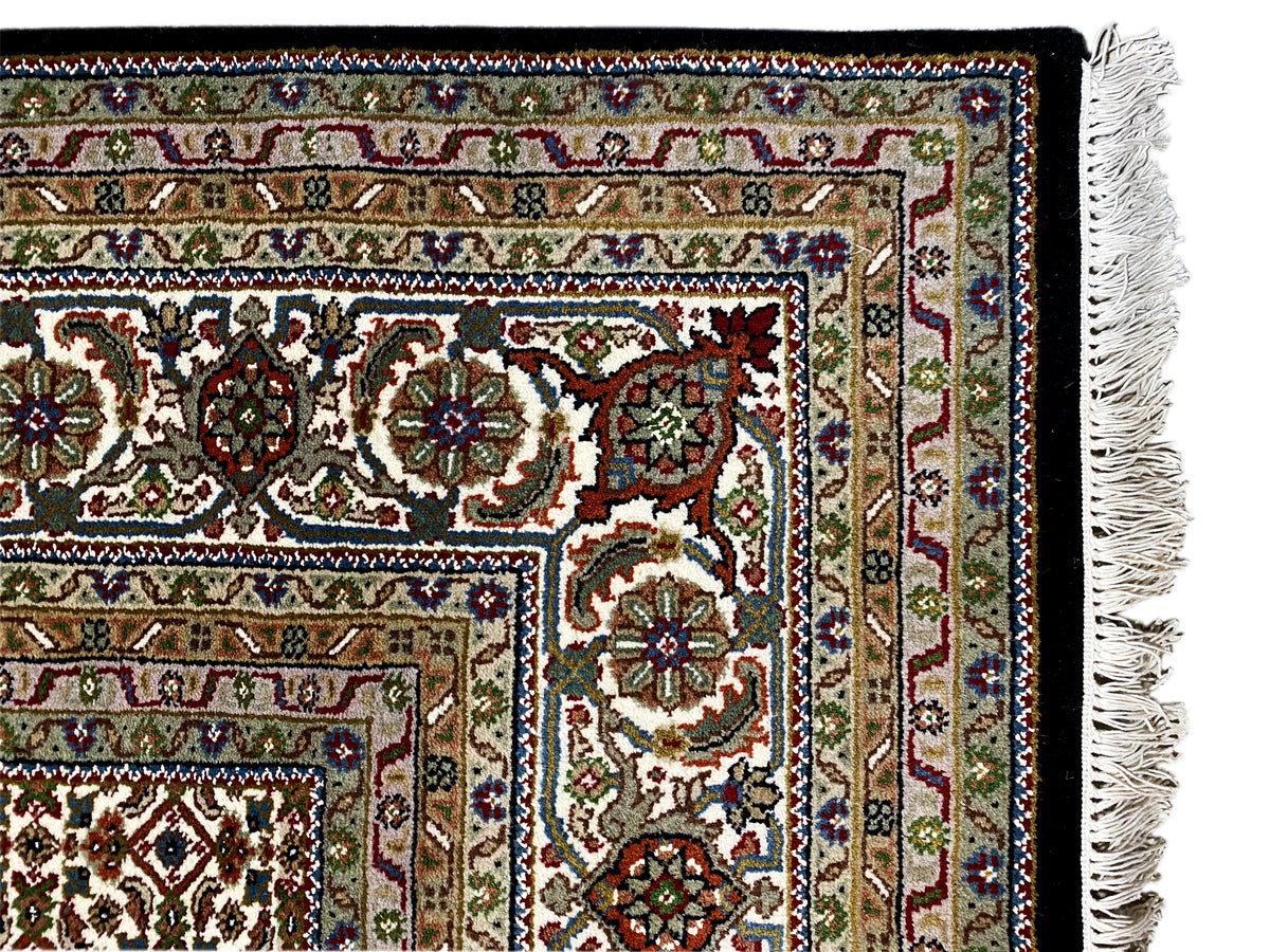 Primer plano del borde de una alfombra Indo-Tabriz marrón con motivos florales y flecos.