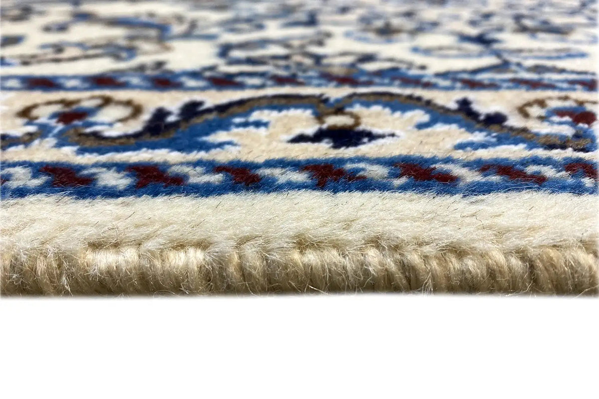 Detalle de la alfombra: flecos en la parte inferior, diseño ornamental azul y blanco, pelo denso