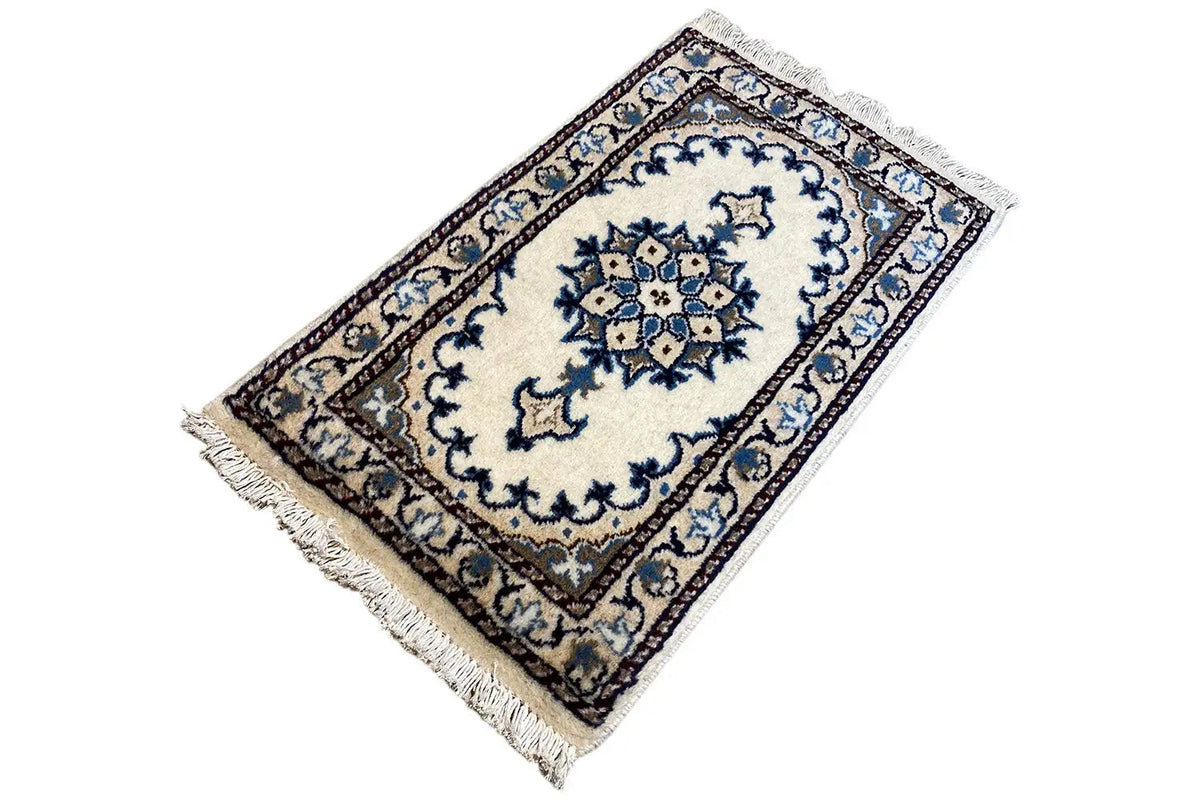 Alfombra oriental de 65x38 cm en vista oblicua con diseño de medallón azul y blanco y flecos
