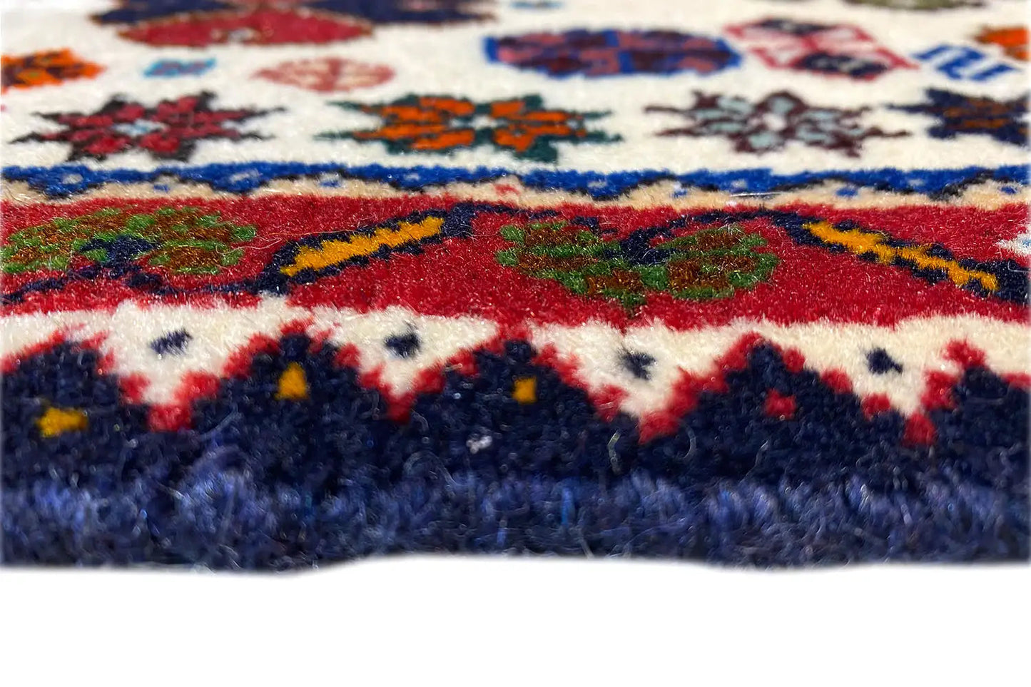 Primer plano: borde de alfombra con flecos; pelo de color crema con franjas de color azul y rojo