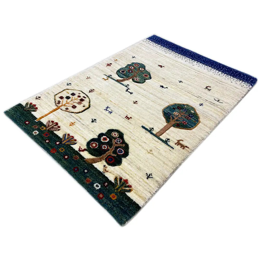 Alfombra Gabbeh vista en diagonal: base color crema, remate azul, motivos de árboles y flores