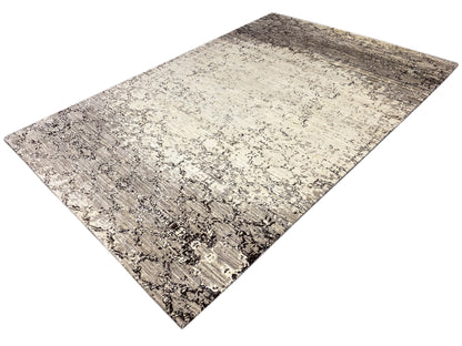 Alfombra con fondo beige claro y manchas gris oscuro, así como líneas ornamentales diagonales