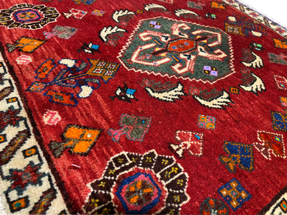 Vista de cerca de una alfombra Poshti de 58x57 cm, con un diseño rojo con motivos de animales y flores