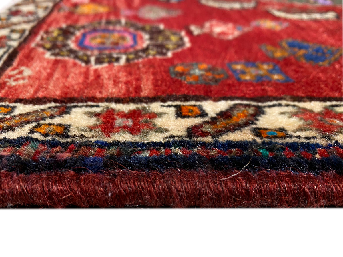 Detalle de la alfombra persa de 58x57 cm: pelo rojo, borde con motivos coloridos y flecos cortos