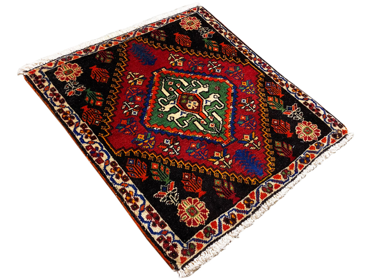 Alfombra poshti de 56x56 cm, colocada en diagonal, con ornamentos geométricos en rojo, verde y azul