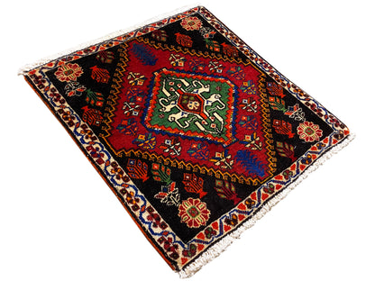 Alfombra poshti de 56x56 cm, colocada en diagonal, con ornamentos geométricos en rojo, verde y azul