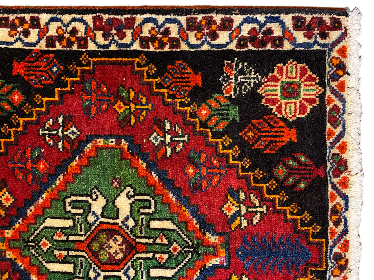 Vista de cerca de la alfombra Poshti: alfombra negra con medallón verde y adornos multicolores