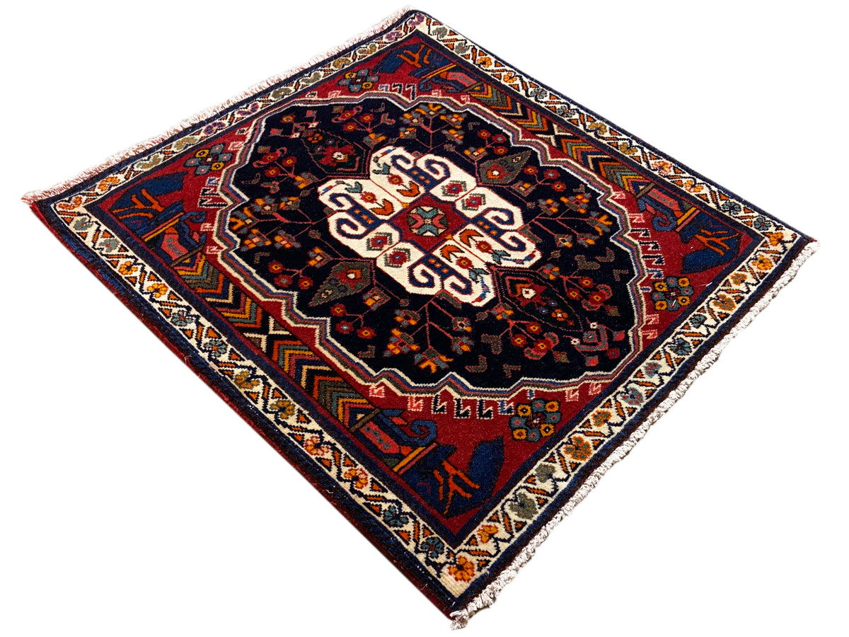 Alfombra Poshti con diseño de rombos, fondo oscuro y ornamento central blanco