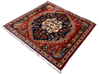 Alfombra Poshti con fondo rojo, medallón oscuro y cenefa perimetral multicolor