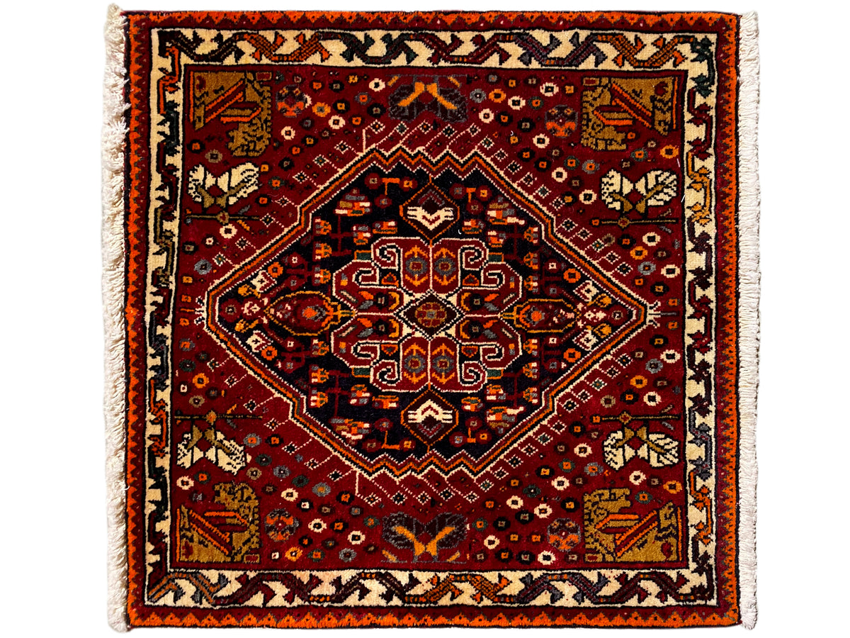 Alfombra Poshti de 60x60 cm, con un patrón ornamental cuadrado en rojo y un borde claro