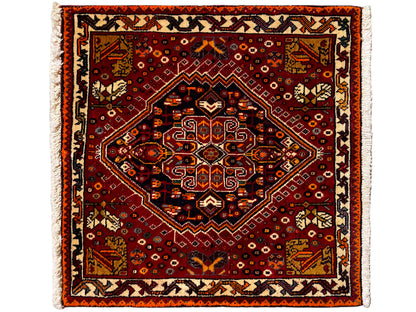Alfombra Poshti de 60x60 cm, con un patrón ornamental cuadrado en rojo y un borde claro