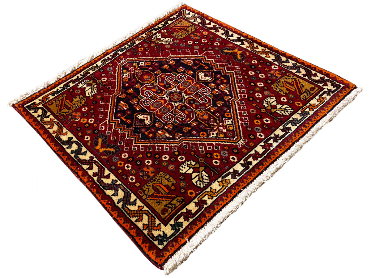 Alfombra Poshti de 60x60 cm, con un diseño de borde rojo, medallón central oscuro y flecos
