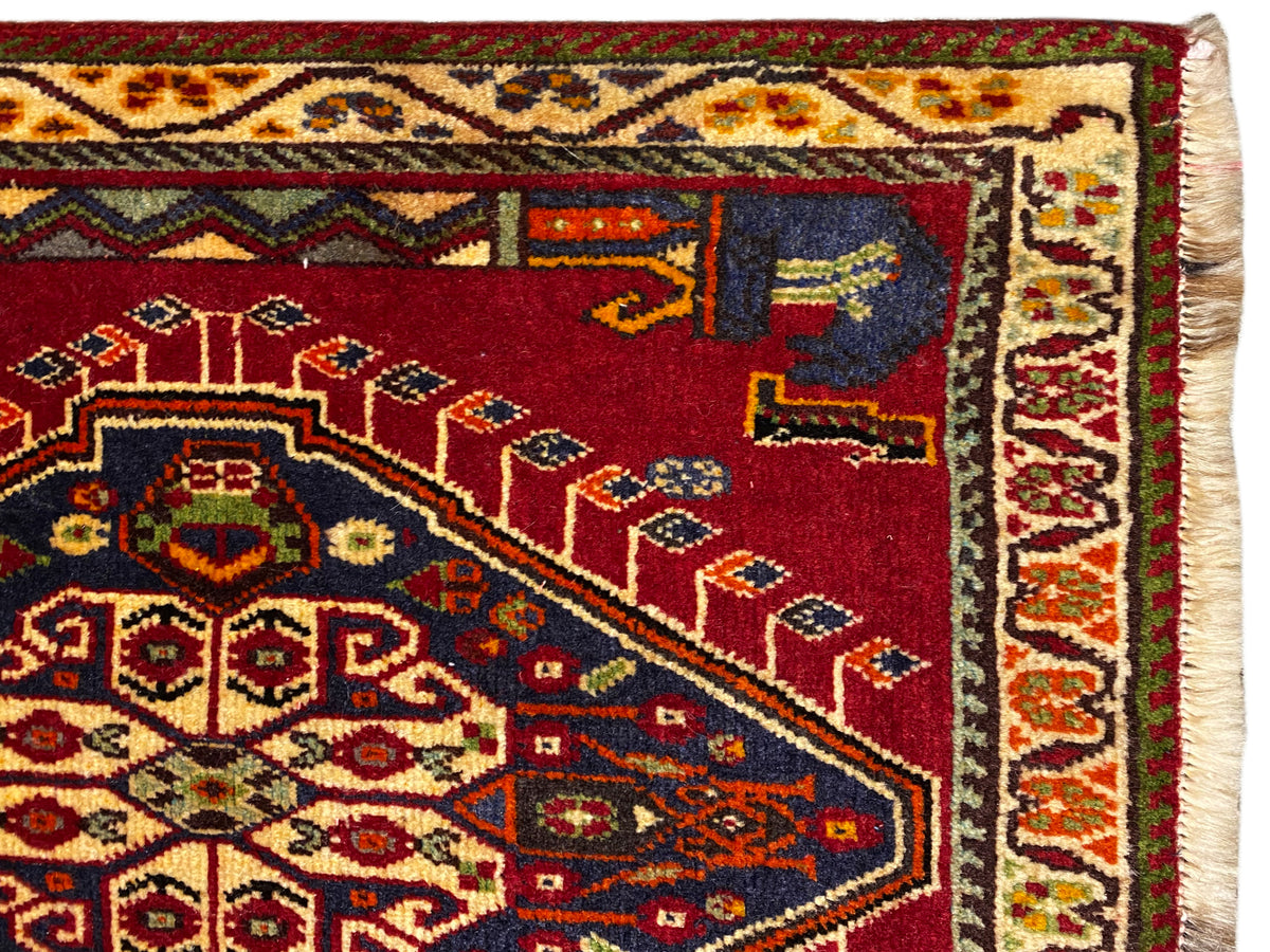 Detalle de la alfombra Poshti (59×61 cm): campo rojo con motivos ornamentales de alfombra y borde ribeteado