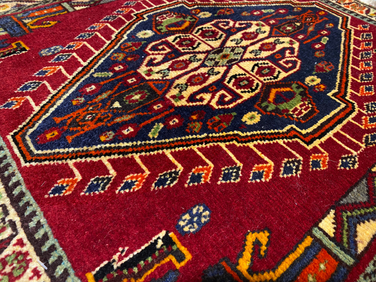 Primer plano de la alfombra Poshti (59×61 cm): patrón interior rojo con ornamentos multicolores y marco