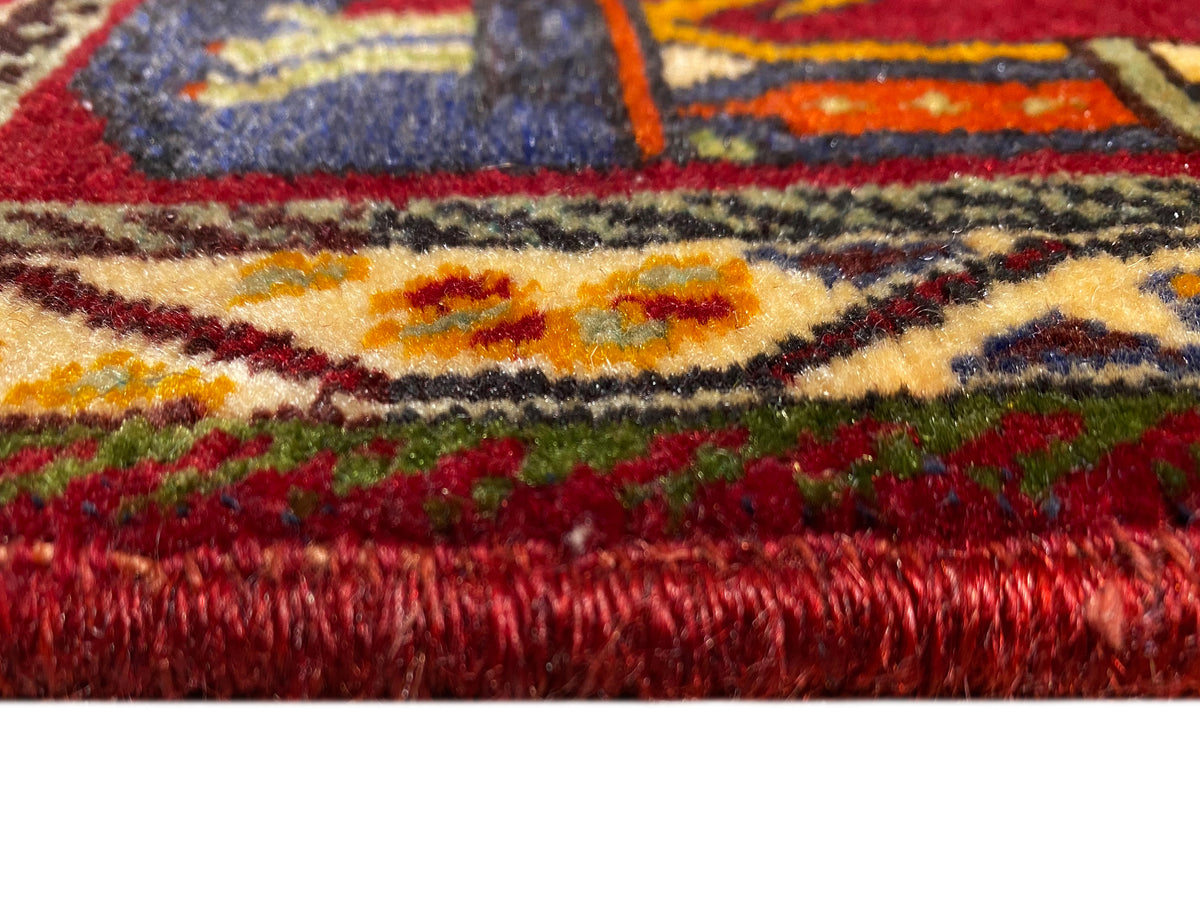 Primer plano de la alfombra Poshti (59×61 cm): pelo rojo y bordes coloridos con flecos