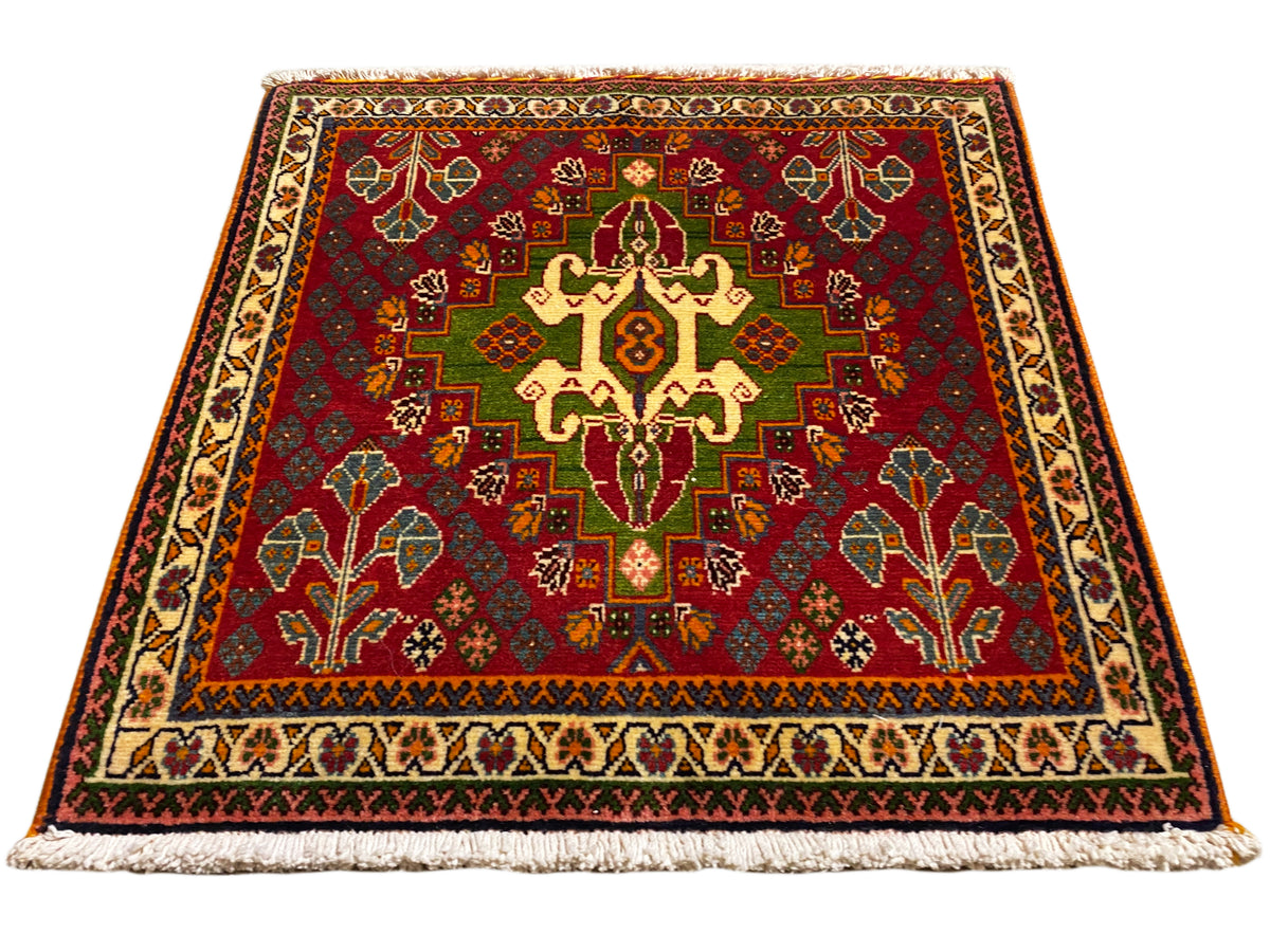 Alfombra oriental con motivo central rojo, detalles verdes y borde beige, con flecos