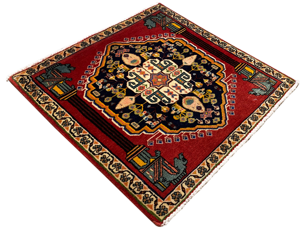 Alfombra Poshti con diseño de rombos, fondo rojo, medallón oscuro y ornamentos en las esquinas