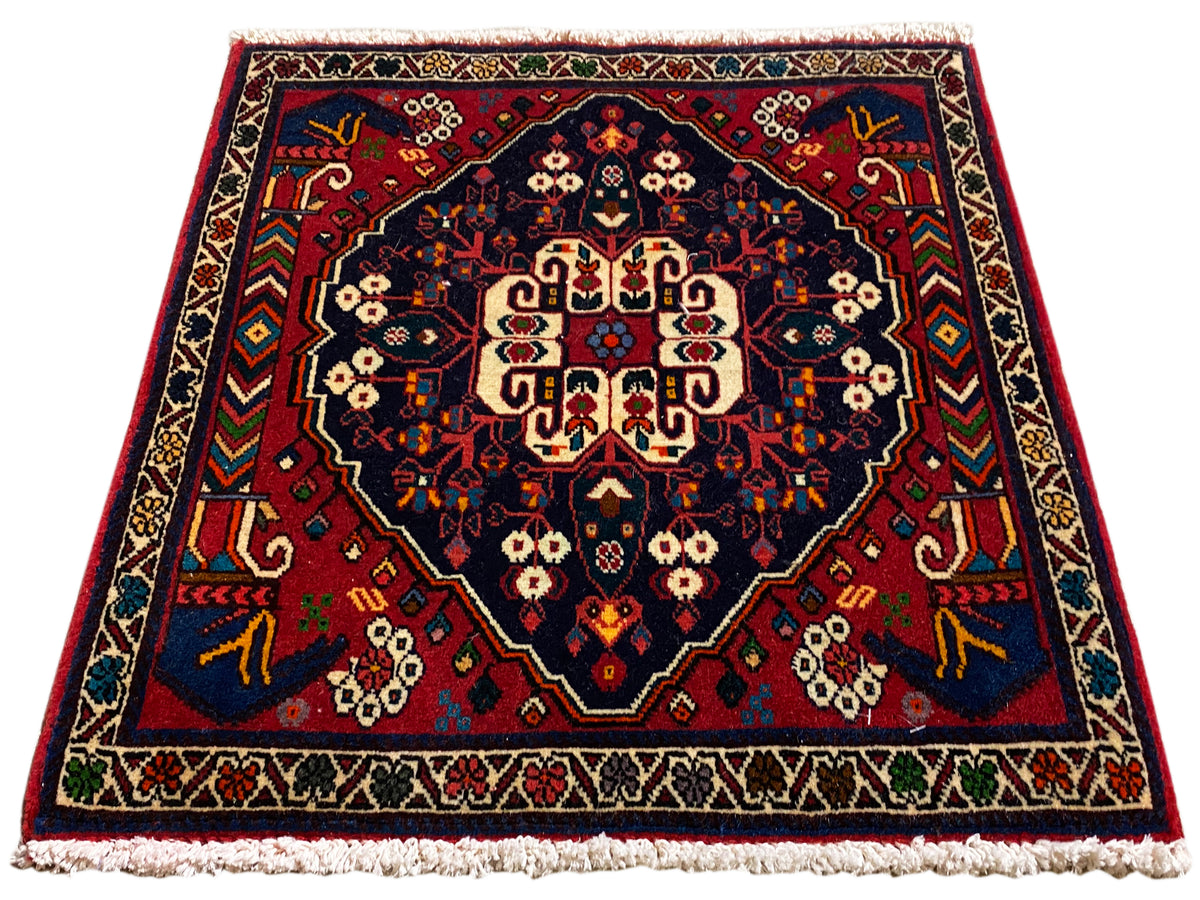 Alfombra cuadrada con medallón central, ornamentación en rojo y azul y flecos cortos