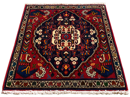 Alfombra cuadrada con medallón central, ornamentación en rojo y azul y flecos cortos