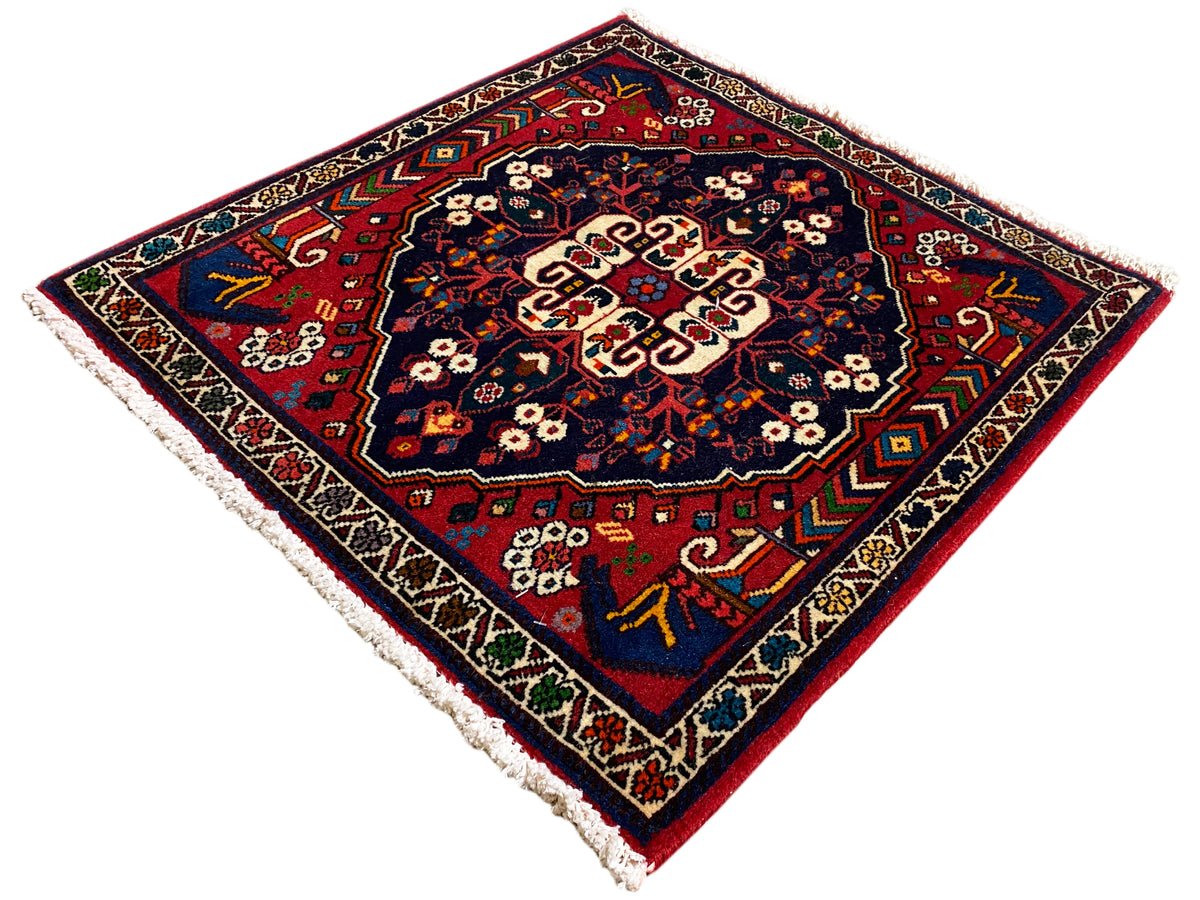 Alfombra cuadrada con ornamento de colores, superficie azul oscuro, motivos en el borde, flecos