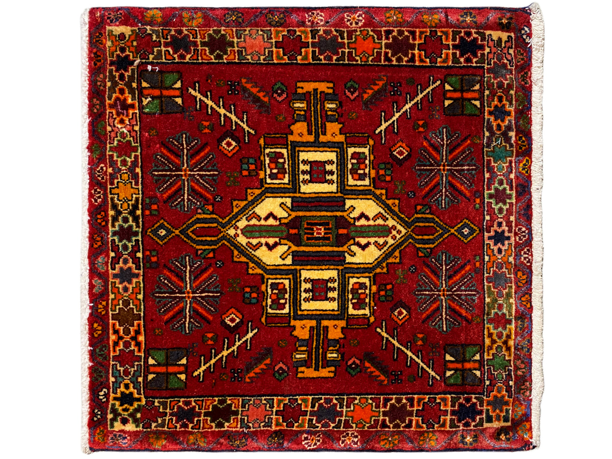 Alfombra Poshti rectangular con fondo rojo y motivo central geométrico, multicolor