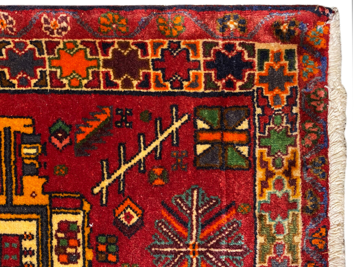 Primer plano: alfombra Poshti con fondo rojo, ornamentos coloridos y cenefa multicolor