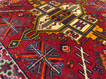 Primer plano: alfombra Poshti con fondo rojo y motivos geométricos coloridos