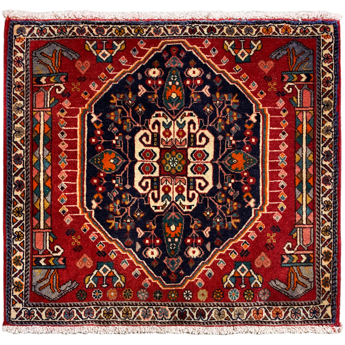 Alfombra cuadrada con fondo rojo y motivo central azul oscuro, con flecos