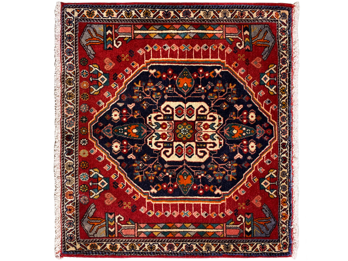 Alfombra con fondo rojo, medallón azul oscuro y cenefa multicolor, cuadrada