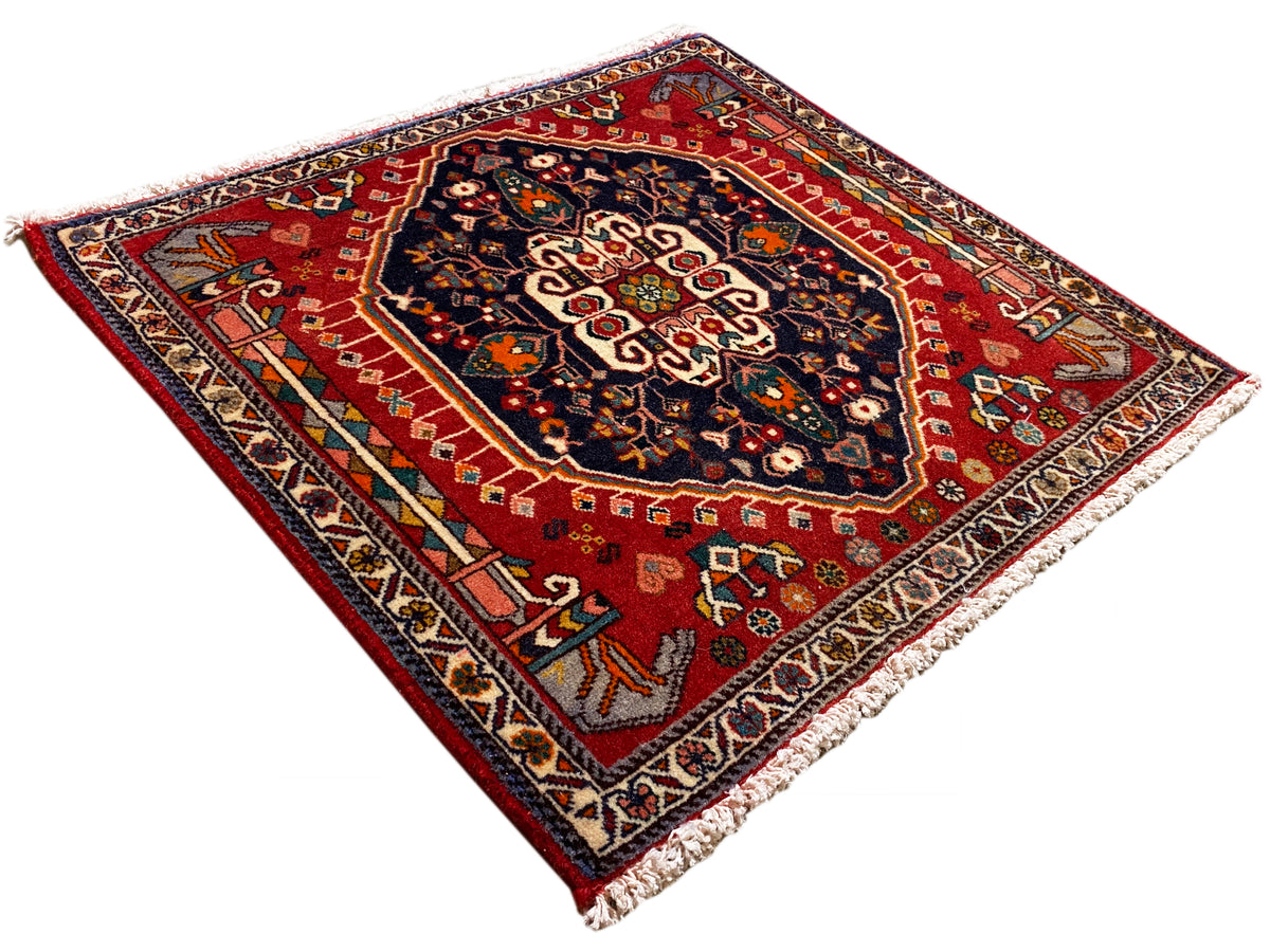 Alfombra rectangular con fondo rojo y motivos ornamentales azules, con flecos