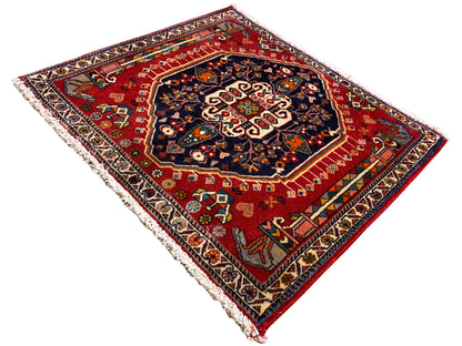 Alfombra de fondo rojo y medallón central oscuro, rectangular, rematada con flecos