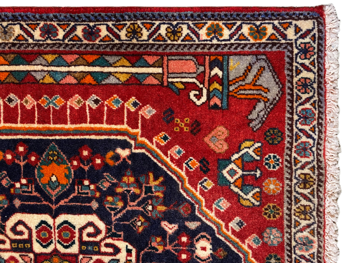 Detalle de alfombra: campo ornamental rojo y azul con cenefa multicolor y flecos