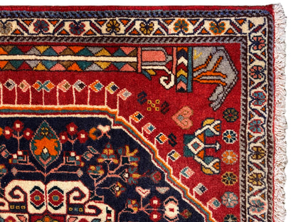 Detalle de alfombra: campo ornamental rojo y azul con cenefa multicolor y flecos