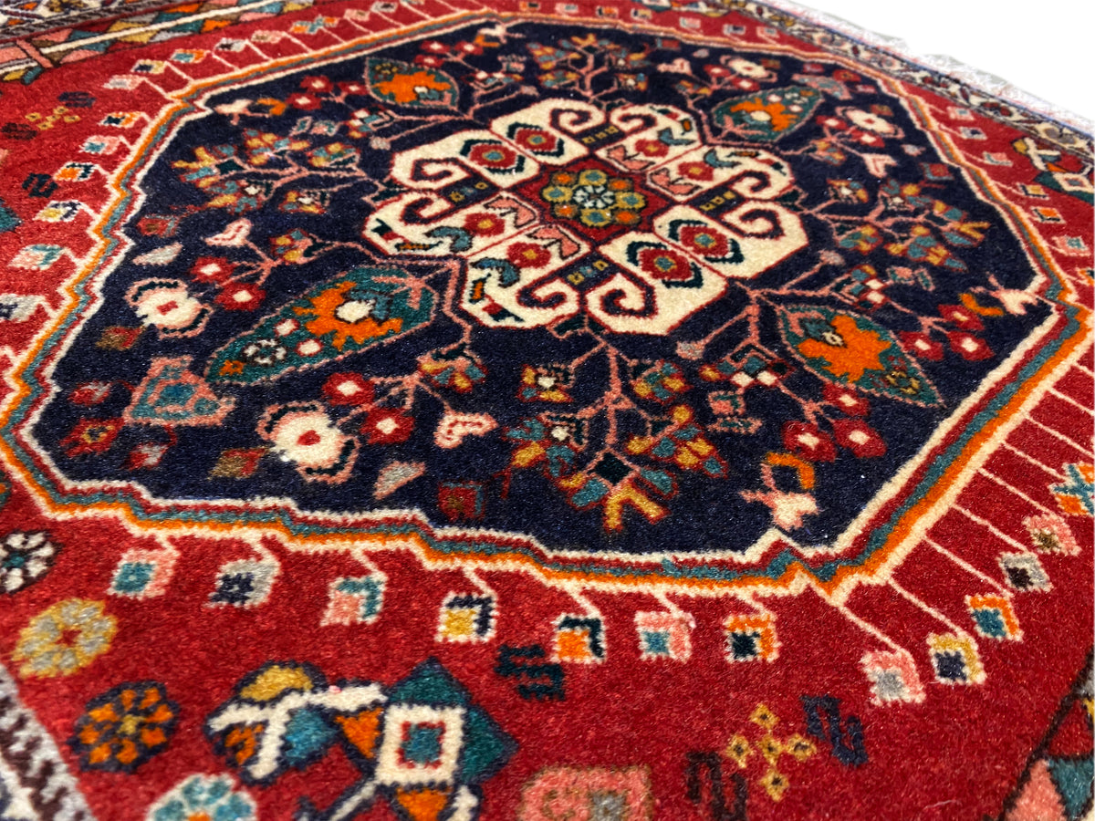 Superficie de la alfombra: ornamento central sobre fondo azul oscuro, cenefa de colores, borde con flecos