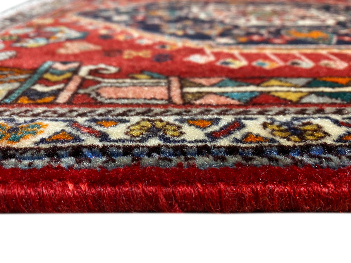Borde de alfombra en detalle: pelo rojo, cenefa de motivos multicolor y flecos deshilachados