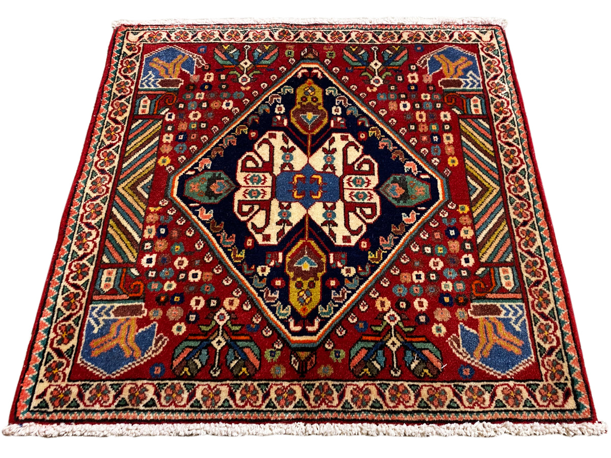 Alfombra de 66x62 cm con estampado rojo, marco oscuro y ornamentos de colores