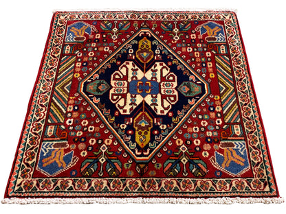 Alfombra de 66x62 cm con estampado rojo, marco oscuro y ornamentos de colores