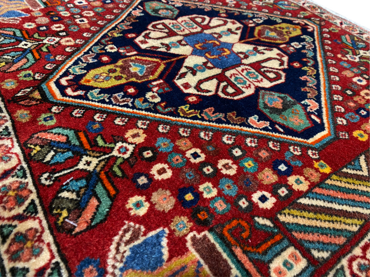 Detalle de la alfombra: rombos coloridos y motivos florales sobre fondo rojo